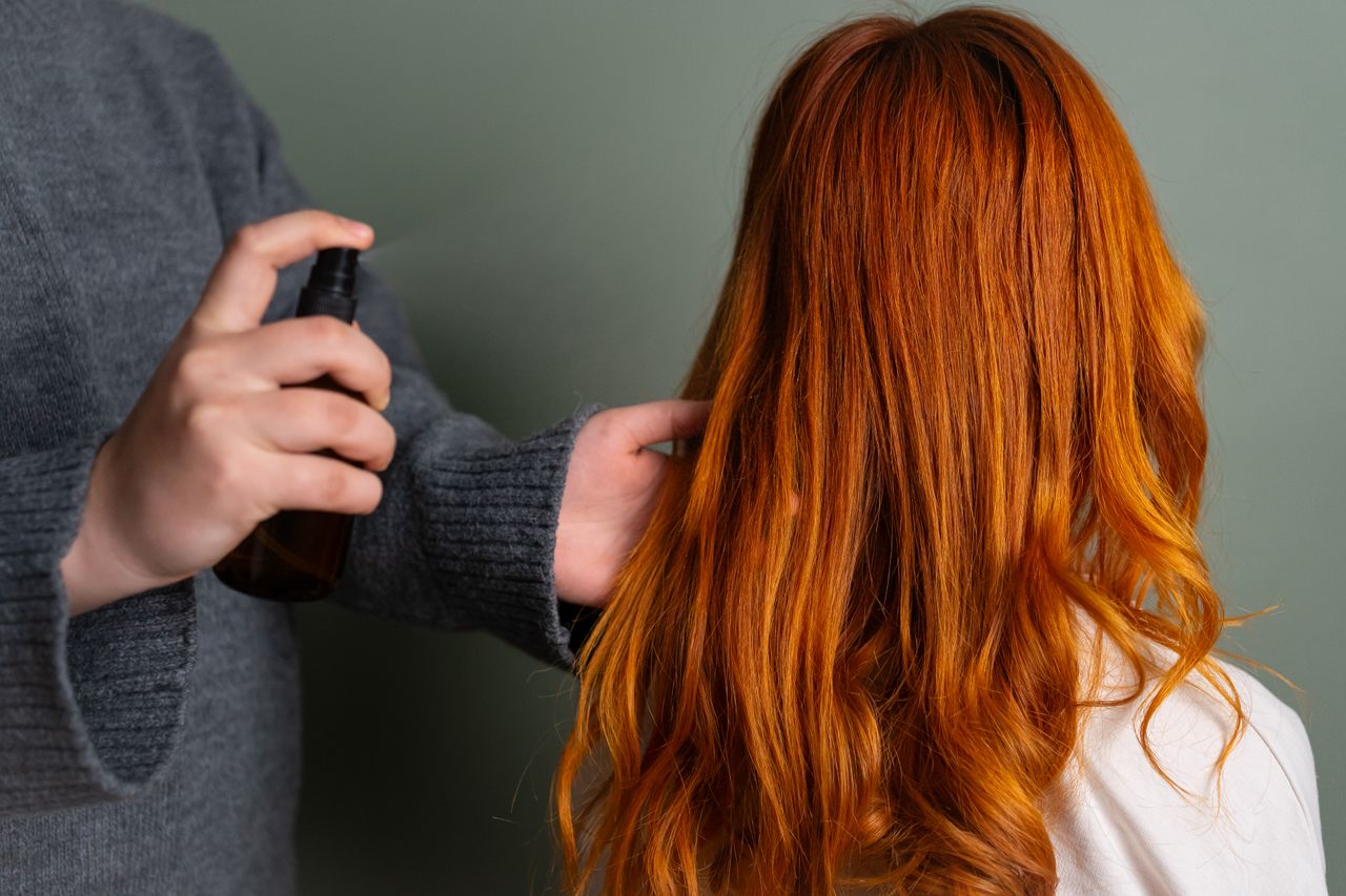 Close-up of hairdresser spraying hair product on long red hair.